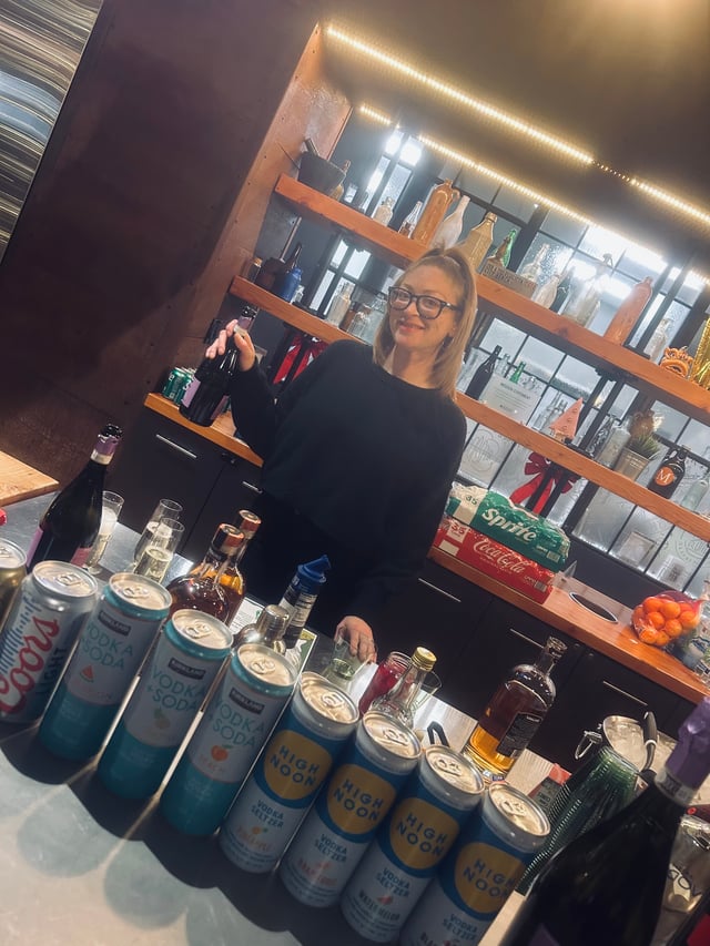 A smiling Bartenders Express bartender behind a modern bar stocked with seltzers